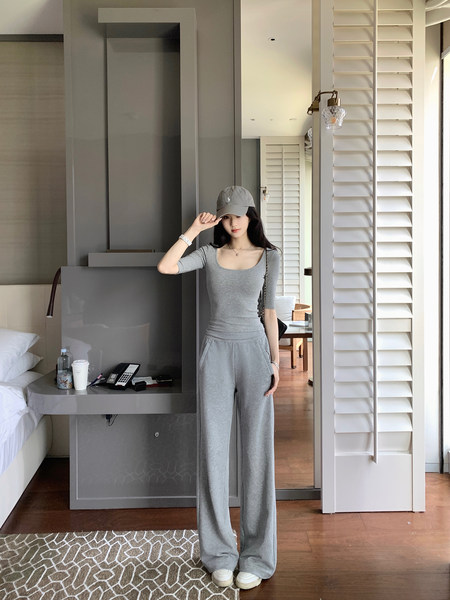 Woman wearing a gray loungewear set with a cap, standing in a modern room.