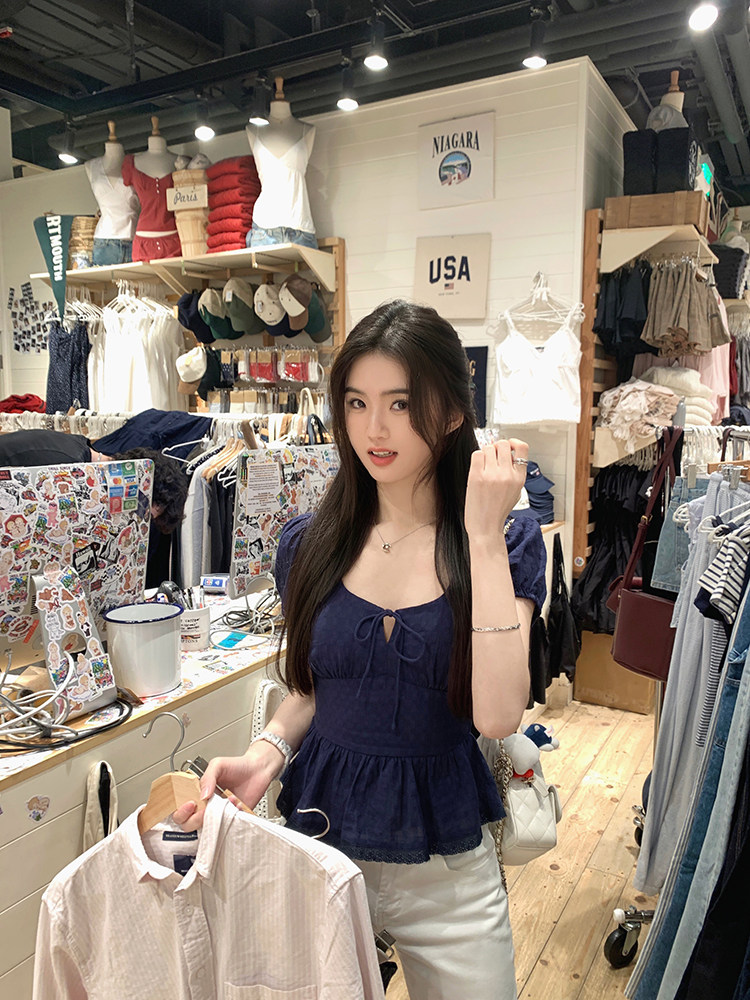 Woman wearing a navy blue top in a clothing store, holding a shirt on a hanger.