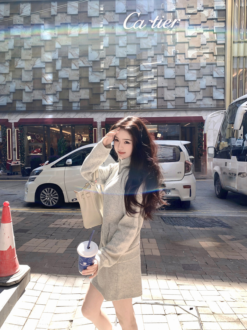 Woman wearing a beige knit dress outdoors in front of a Cartier store, holding a drink and a handbag.
