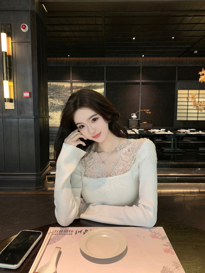 Woman wearing a white long-sleeve top with lace detailing, seated at a restaurant table