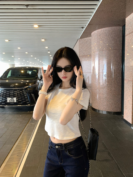 Woman wearing white crop top and jeans with sunglasses and a black bag