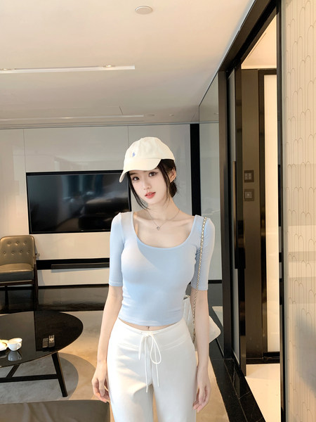 Woman wearing light blue fitted top and white pants with a white cap