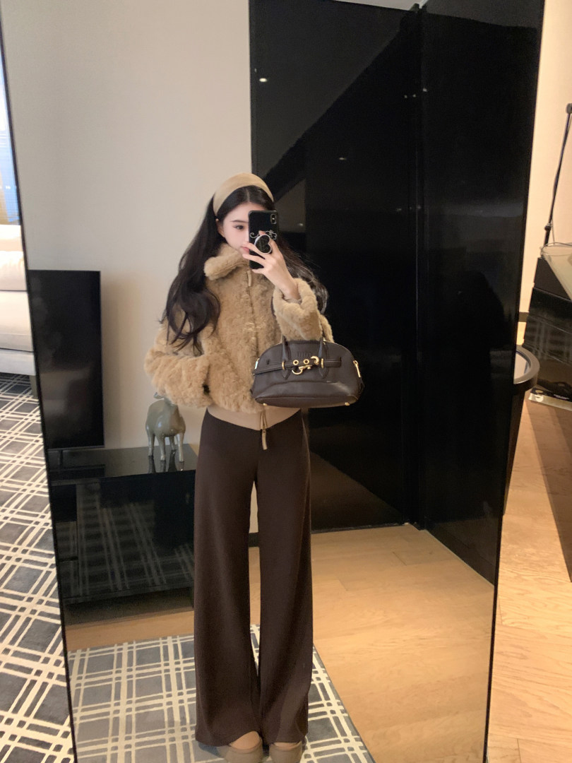 Woman wearing a beige fluffy jacket, brown wide-leg pants, and holding a brown handbag while taking a mirror selfie.