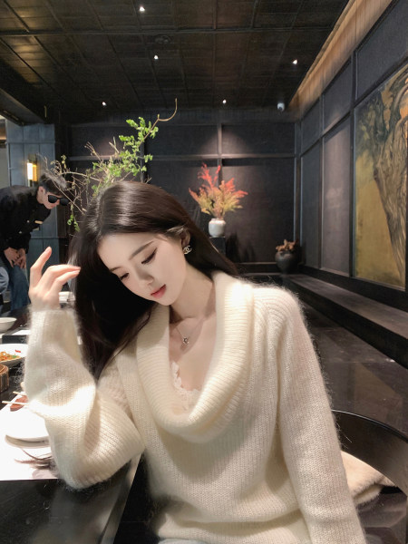 Woman wearing a cream-colored knit sweater with a deep V-neck and lace trim, seated in a dimly lit restaurant.