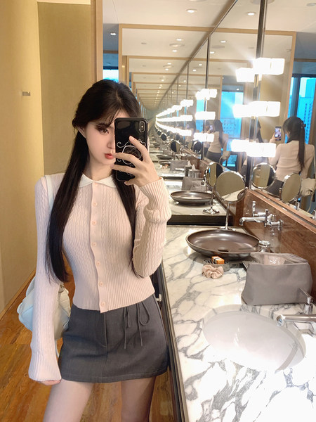 Woman taking mirror selfie wearing ribbed cardigan and gray skirt in bathroom