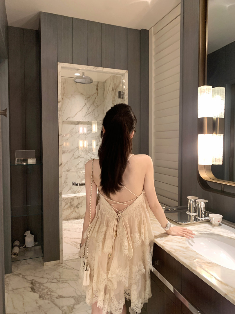 Woman wearing a lace dress with crisscross back detailing in a luxurious bathroom