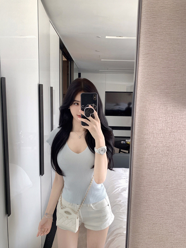 Woman taking mirror selfie wearing light blue ribbed top and white shorts with a small white handbag.