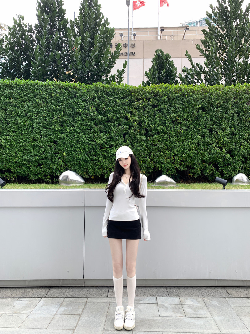 Woman wearing white long-sleeve top, black mini skirt, white socks, and sneakers outdoors