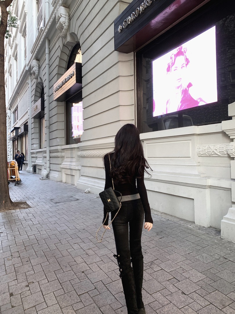 Woman wearing black outfit and carrying a black quilted handbag with chain strap, walking on a city street.
