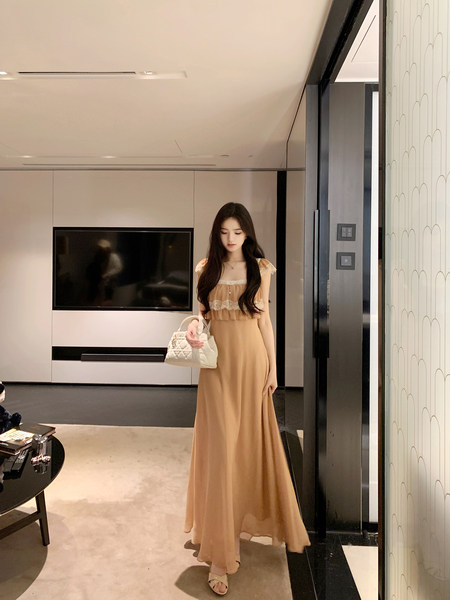 Woman wearing a beige long dress with lace details, holding a white handbag.