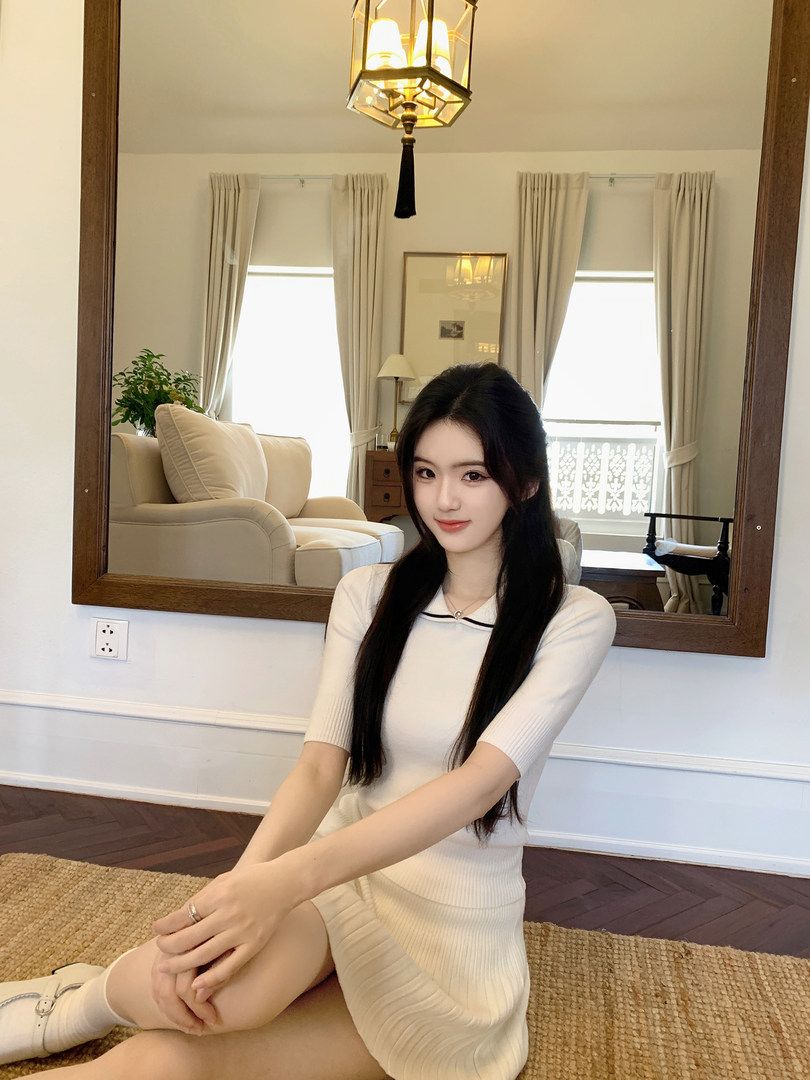 Woman wearing a white ribbed knit dress with black trim, sitting on a rug in a well-lit room