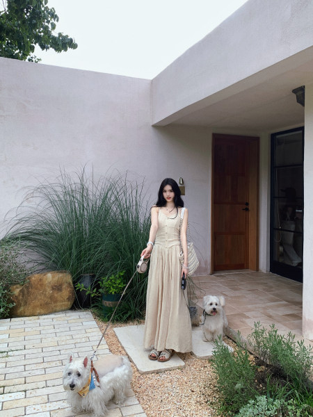 Woman wearing a beige sleeveless dress with two dogs in a courtyard setting