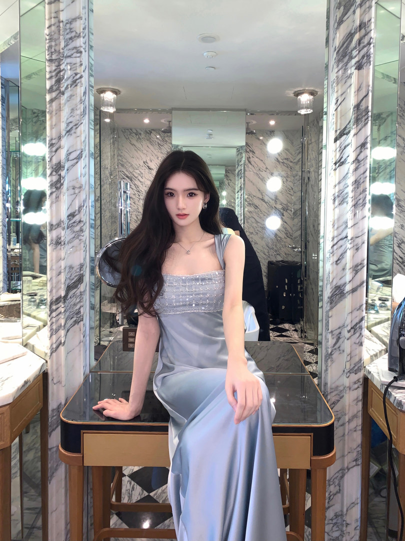 Woman wearing a light blue satin dress with embellished bodice, seated in a luxurious marble room.