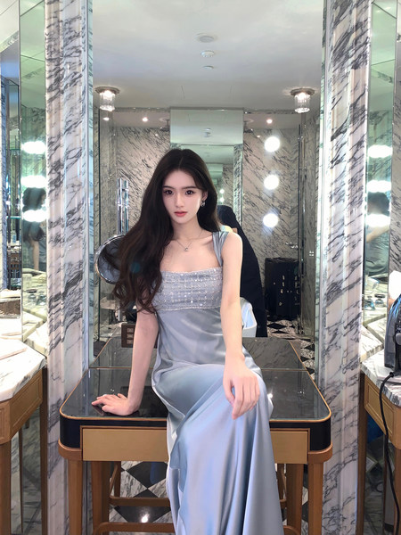 Woman wearing a light blue satin dress with embellished bodice, seated in a luxurious marble room.
