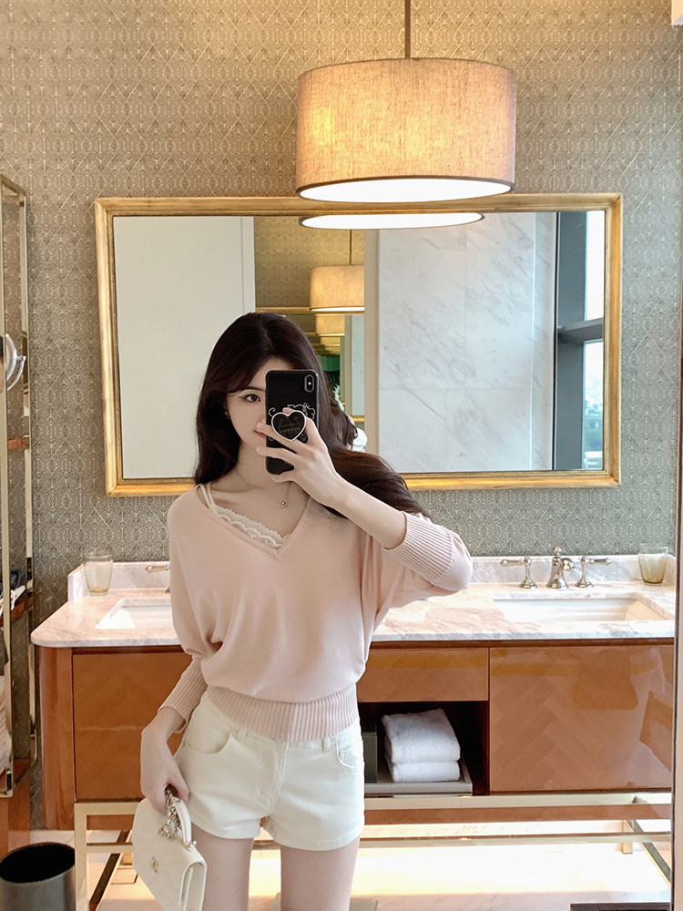 Woman taking mirror selfie wearing a pink V-neck sweater and white shorts.