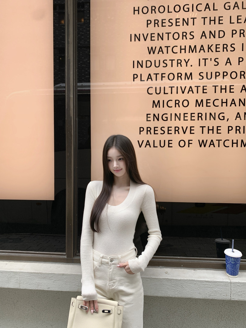 Woman wearing a white ribbed long-sleeve top and matching pants, holding a handbag, standing in front of a window with text overlay.