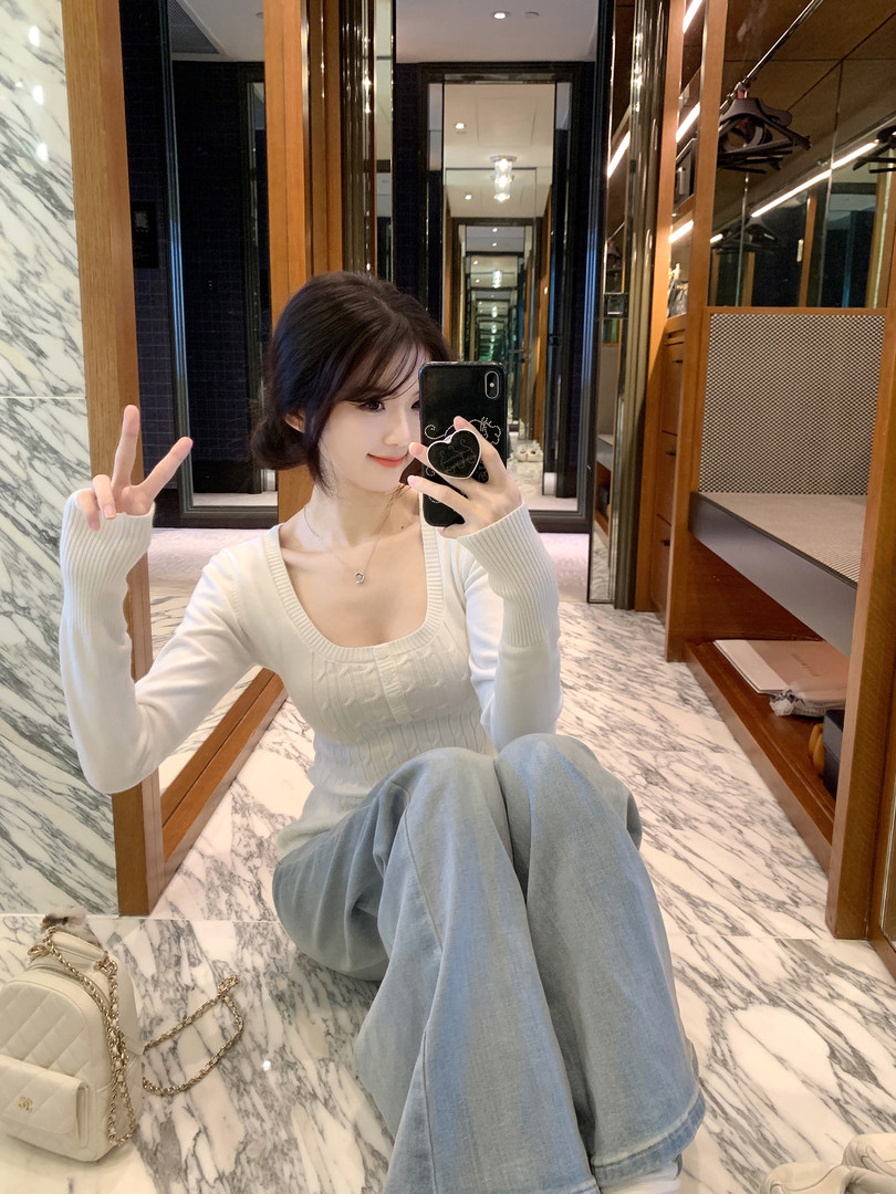Woman taking mirror selfie wearing white ribbed long-sleeve top and light blue wide-leg pants