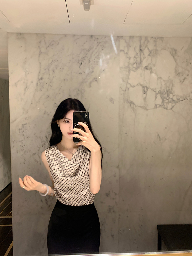 Woman taking mirror selfie wearing a checkered sleeveless top and black skirt