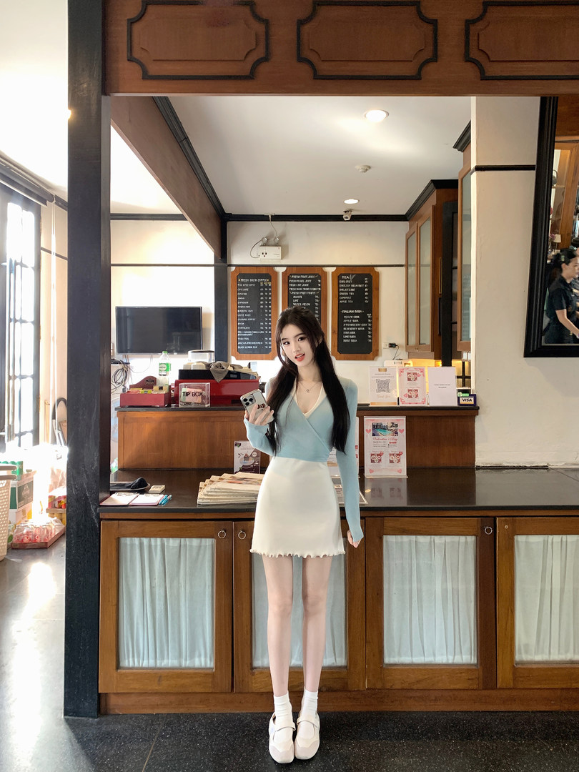 A woman posing in a light blue top and white skirt in a café setting.