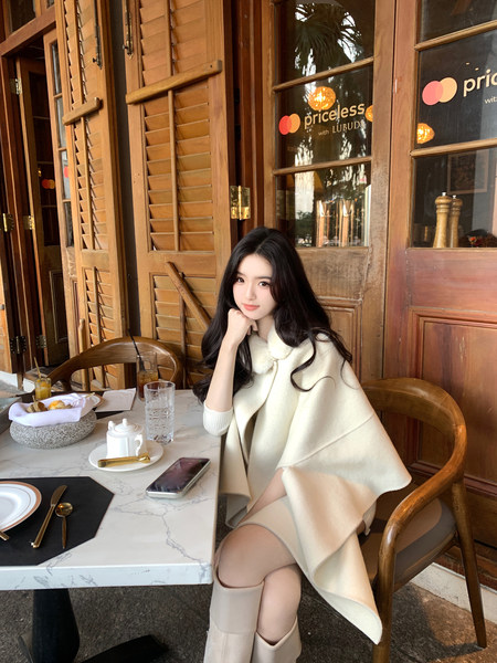 Woman wearing a cream-colored cape-style coat sitting at a café table