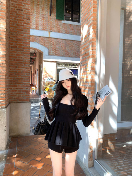 Woman wearing black peplum top and shorts with white hat, standing outdoors near brick building