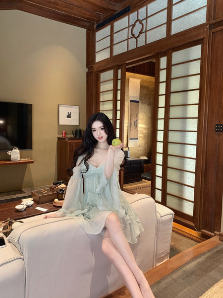 Woman wearing a light blue ruffled dress sitting on a sofa in a traditional-style room