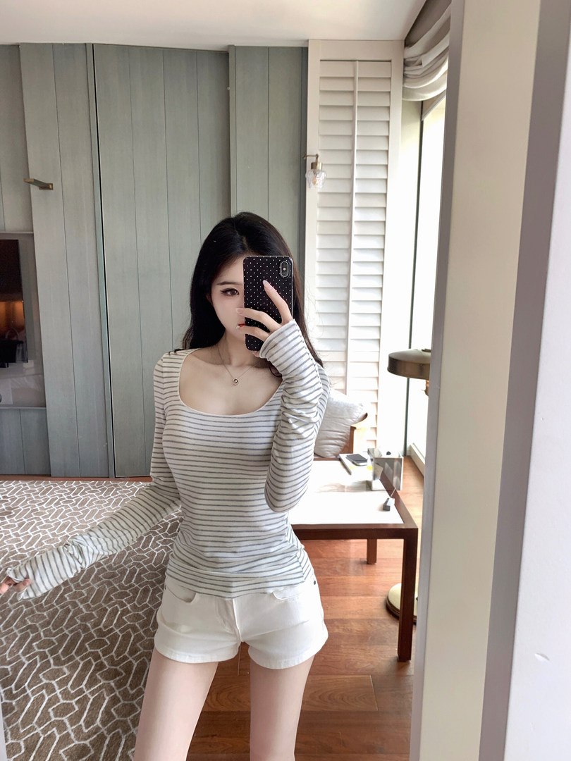 Woman taking mirror selfie wearing striped long-sleeve top and white shorts