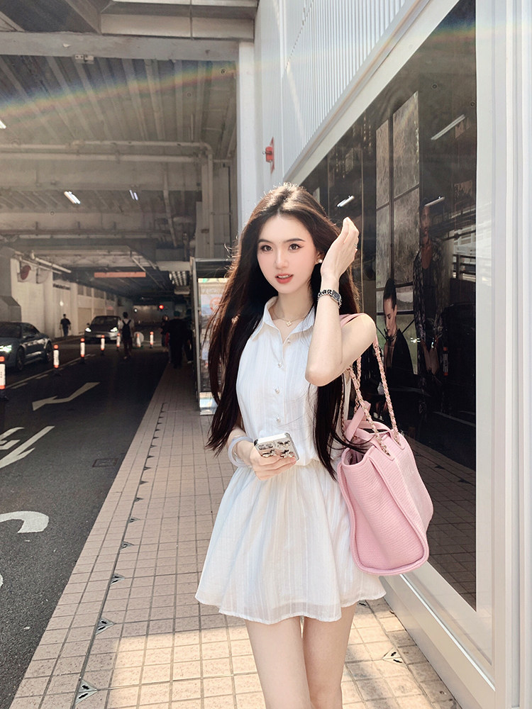 Woman wearing a white button-up dress with a pink handbag, standing outdoors near a building.