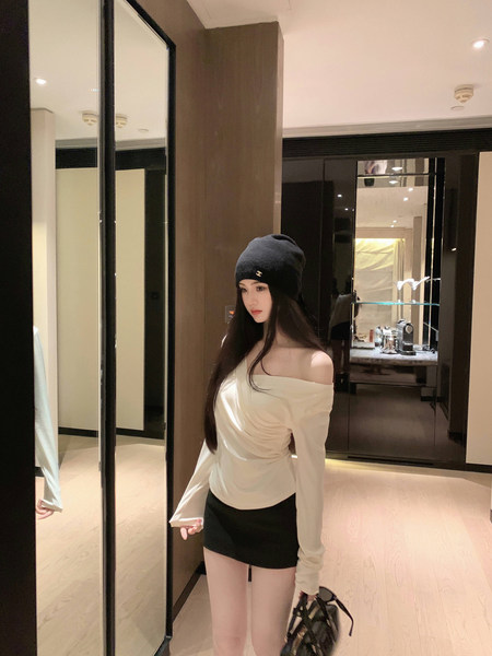Woman wearing off-shoulder white top, black mini skirt, and black beanie with logo, holding handbag in mirrored room