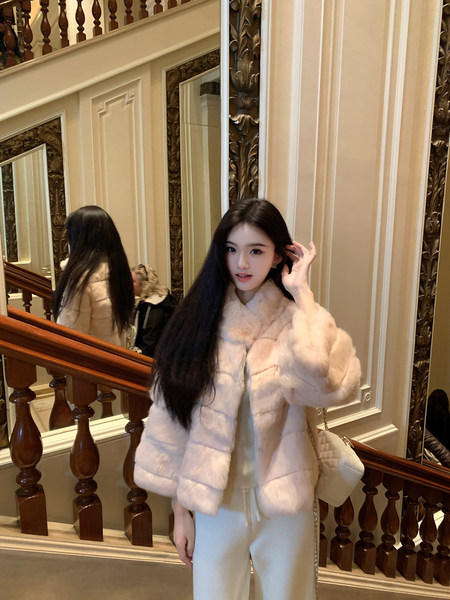 Woman wearing a light pink faux fur coat indoors near a staircase