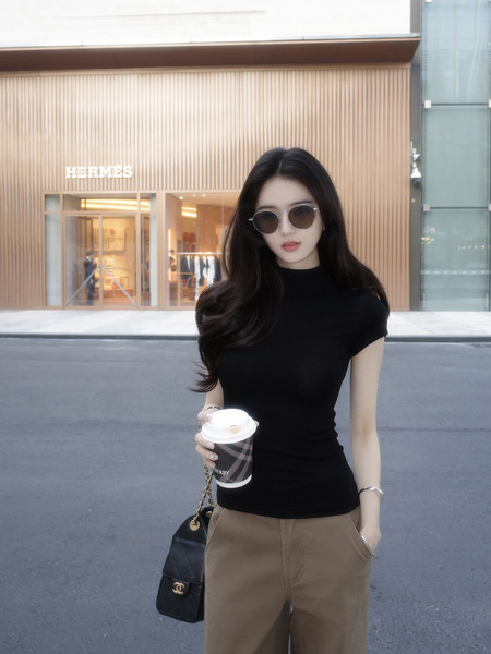 Woman wearing black short-sleeve top and brown pants holding a coffee cup