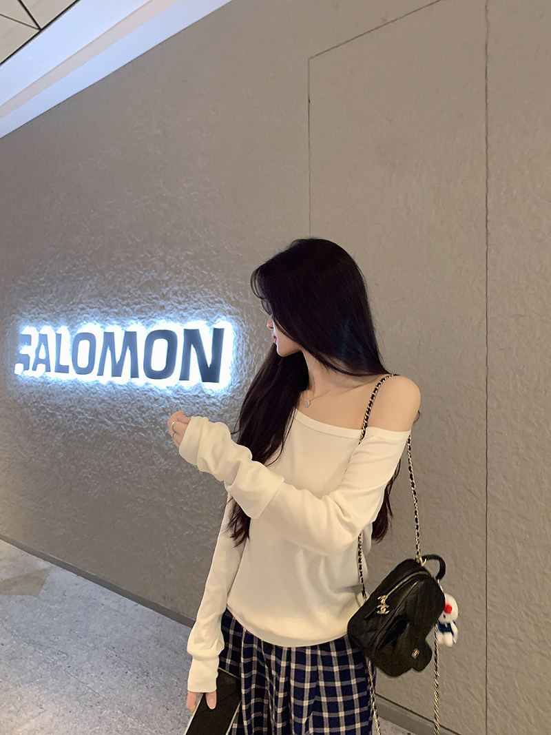 Woman wearing off-shoulder white top and plaid skirt with a black bag, standing near a lit 'BALOMON' sign.
