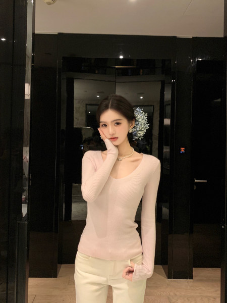 Woman wearing a light pink ribbed long-sleeve top and white pants, posing indoors