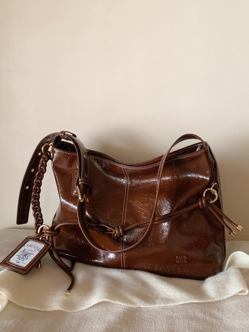 Brown leather shoulder handbag with braided strap and gold hardware on a neutral background