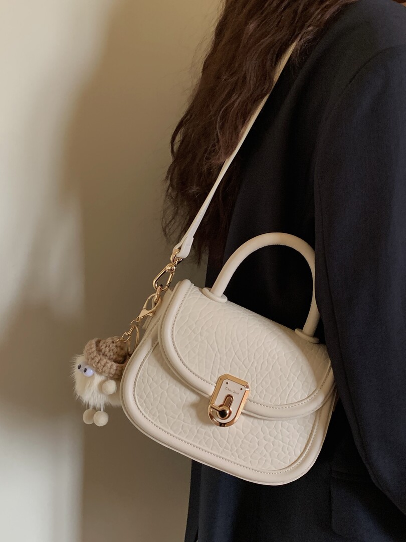 White quilted handbag worn over the shoulder with a charm accessory