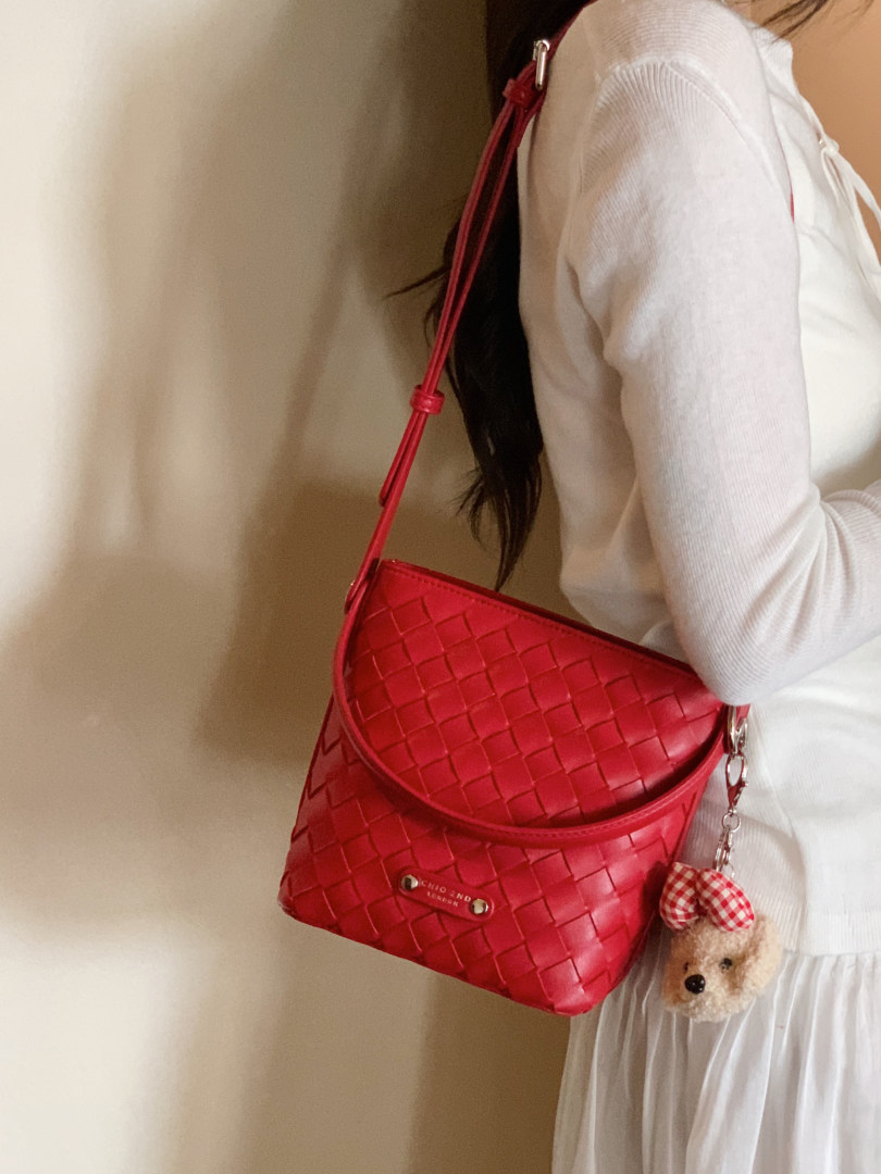 Red woven crossbody handbag worn by a model with a teddy bear charm