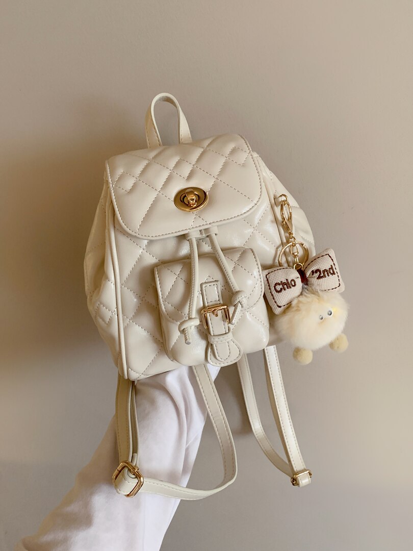 Cream quilted mini backpack with gold hardware and charm accessory