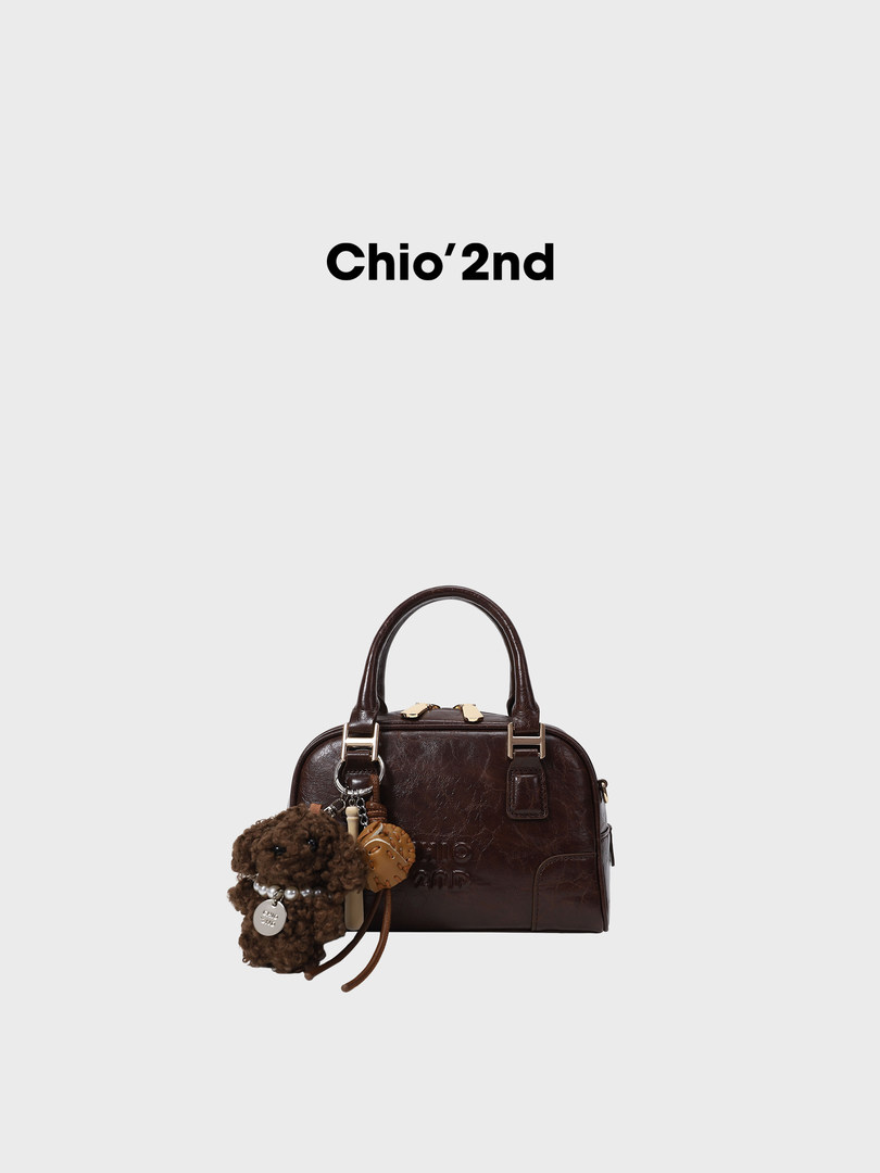 Brown leather handbag with top handle and plush charm on a plain background