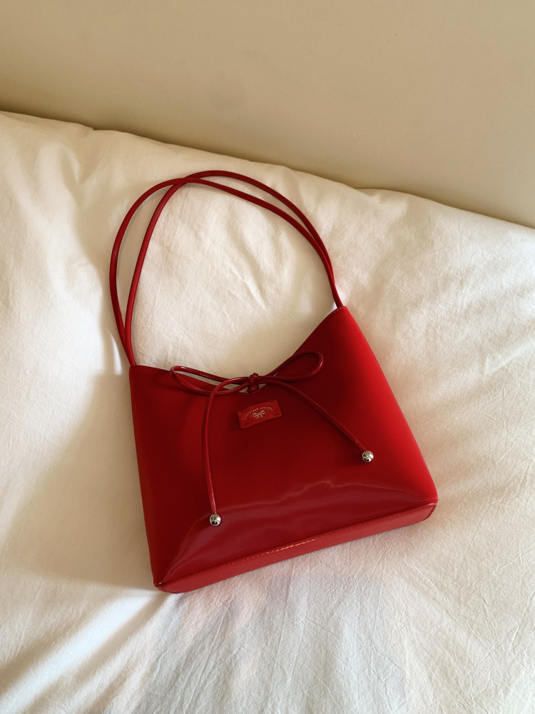 Red leather handbag with long shoulder straps and bow detail on a white bedspread