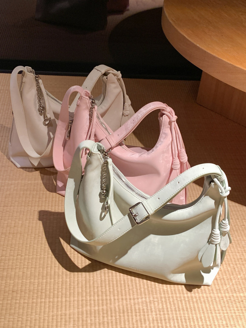 Three small pastel shoulder handbags displayed on a floor