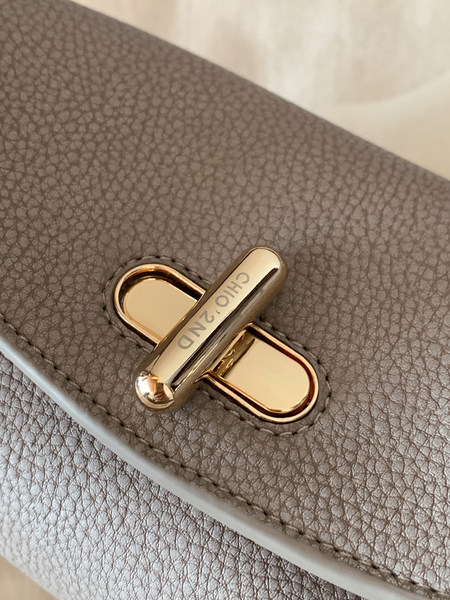 Close-up of a gray pebbled leather handbag clasp with gold hardware