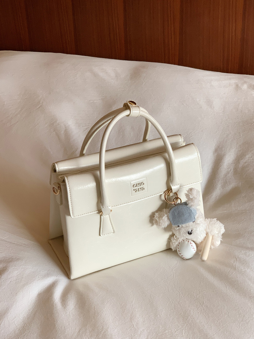 Cream structured leather handbag with top handles and teddy bear charm