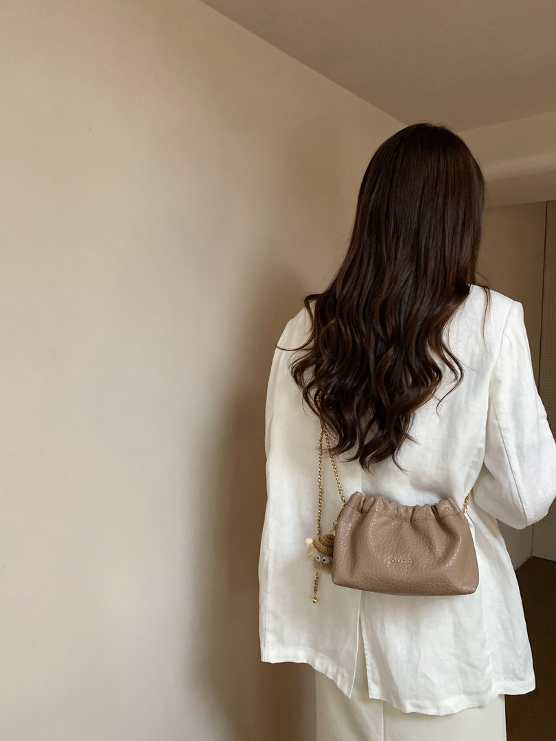 Beige drawstring crossbody bag worn over a white outfit