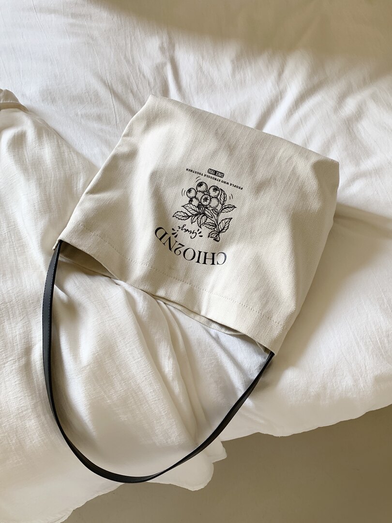 Beige canvas tote bag with black handles and printed graphic on a bed