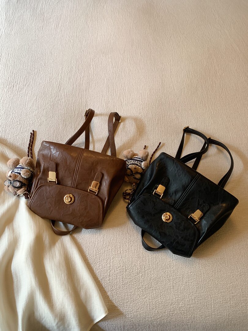 Brown and black leather backpacks displayed on a bed