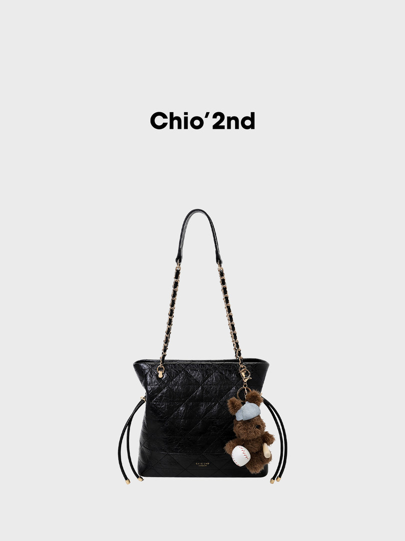 Black quilted chain-strap handbag with teddy bear charm on a plain background