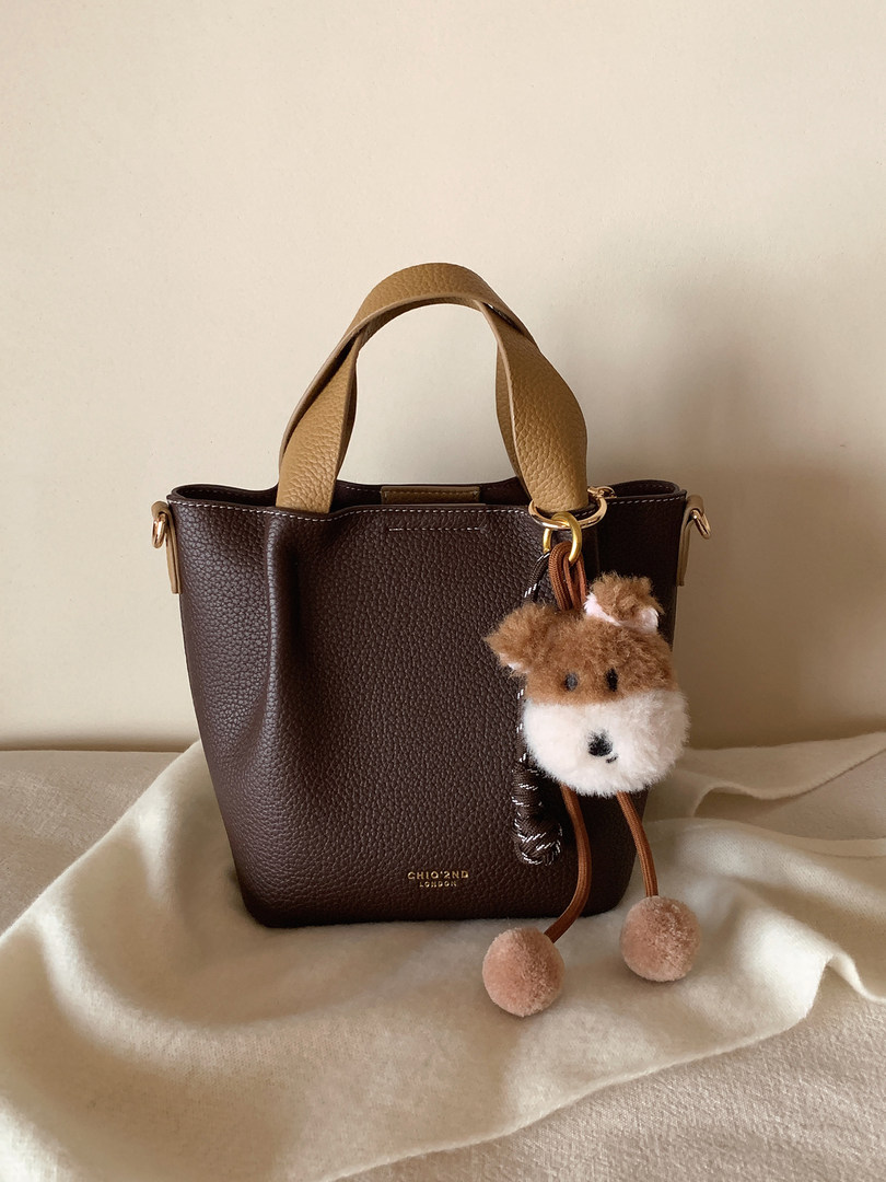 Dark brown pebbled leather tote bag with beige handles and a fluffy animal charm