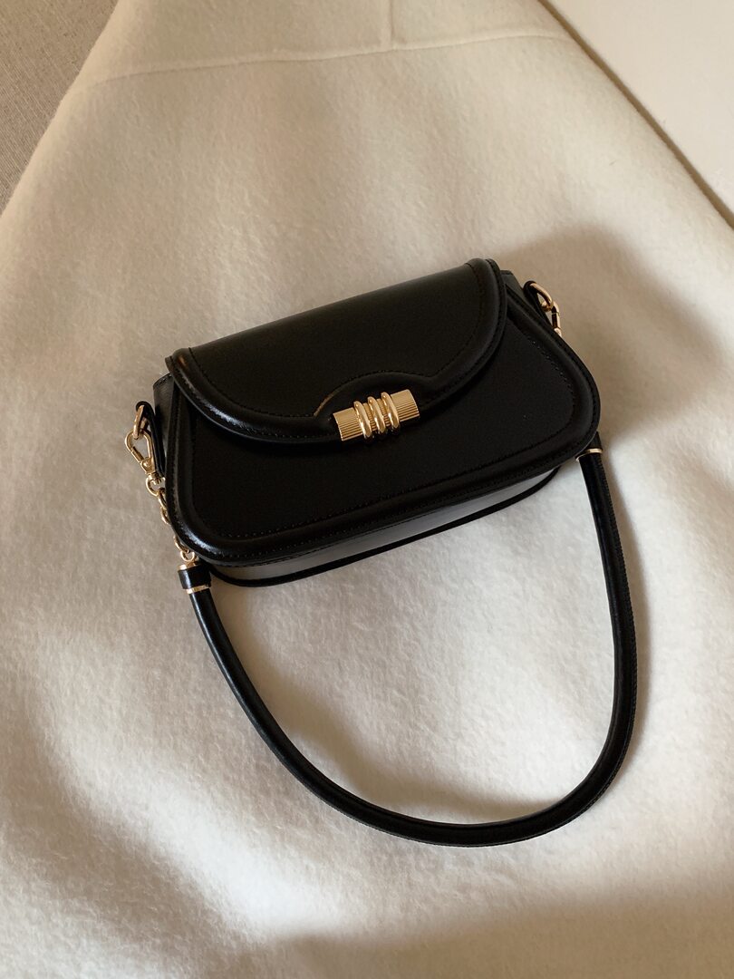 Black leather shoulder bag with gold hardware on a light fabric background