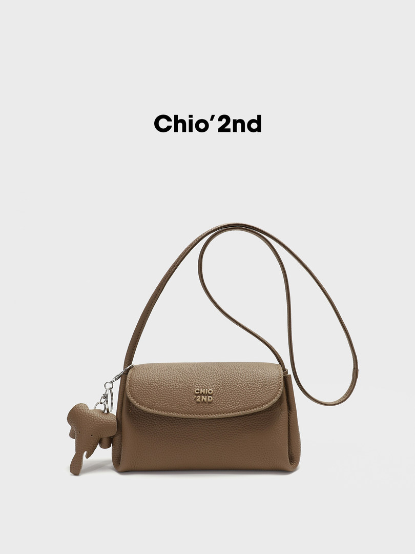 Brown textured crossbody handbag with long strap and charm on white background