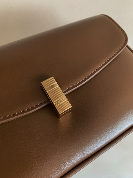 Brown leather handbag with gold clasp on a plain background